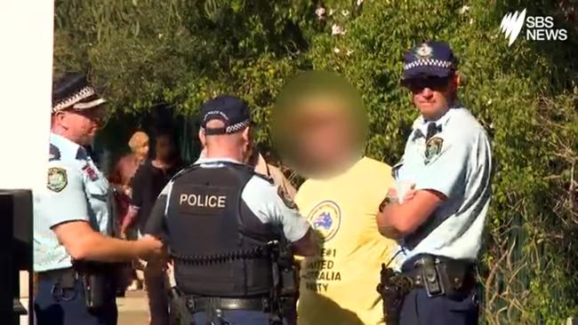 A supporter of Clive Palmer's United Australia Party is spoken to by police and issued a fine for offensive conduct at a polling booth in Bankstown. Picture: SBS