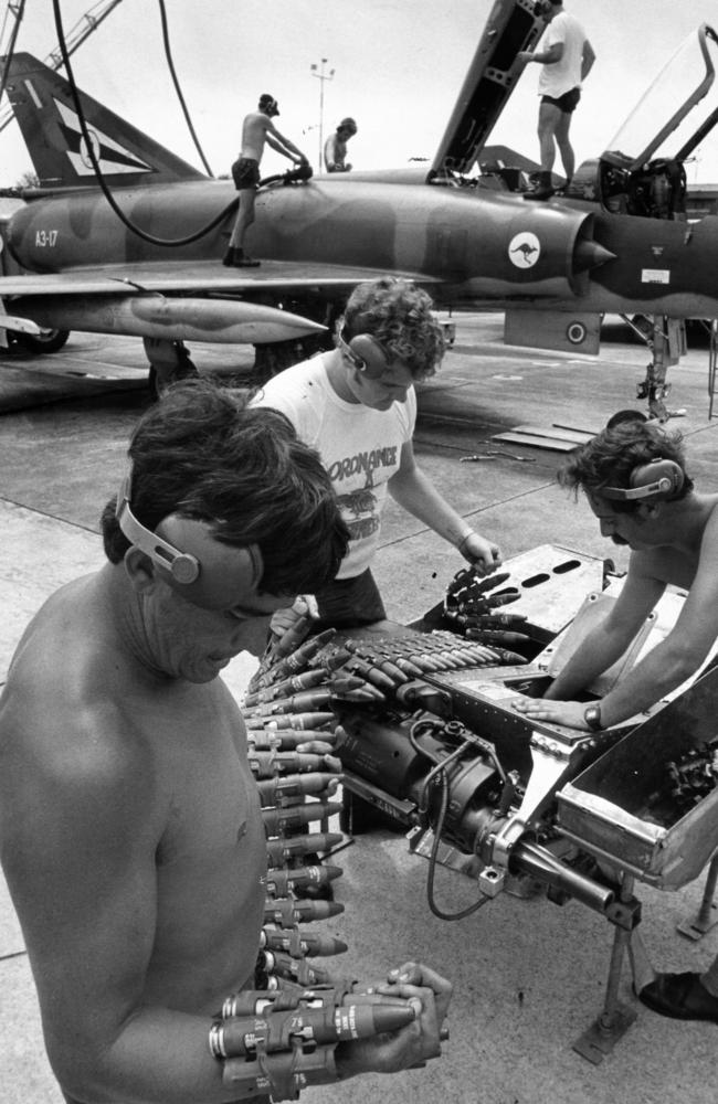 At RAAF Air Base, Butterworth, Penang, Corporal Les Que (left) in charge of this 75 Squadron armament group, feeds a belt of 30mm canon shells to Leading Aircraftman Ian Powell. The shells were to be fired from the Mirage (in the background) at a target banner towed behind a Canberra from RAAF Air Base, Amberley, Qld. Leading Aircraftman Peter Donaghy, 27, of Hobart (right), clears out the empty gun belt links left in a Mirage gun pack.