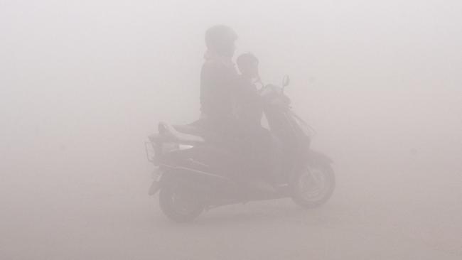 In this Thursday, Nov. 9, 2017, file photo, a woman drives a scooter through the morning fog to drop off a child at school in Greater Noida, near New Delhi, India. A thick gray haze has enveloped India's capital region as air pollution hit hazardous levels. As winter approaches, a thick, soupy smog routinely envelops most parts of northern India, caused by dust, the burning of crops, emissions from factories and the burning of coal and piles of garbage as the poor try to keep warm. (AP Photo/R S Iyer, File)