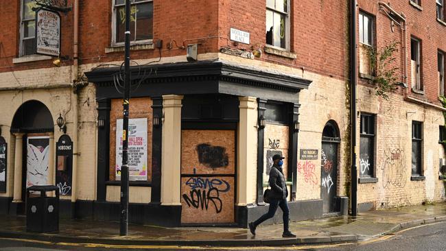 A pedestrian wearing a face mask as a precaution against the transmission of the novel coronavirus walk pasts a derelict pub in Manchester, north west England on October 13.