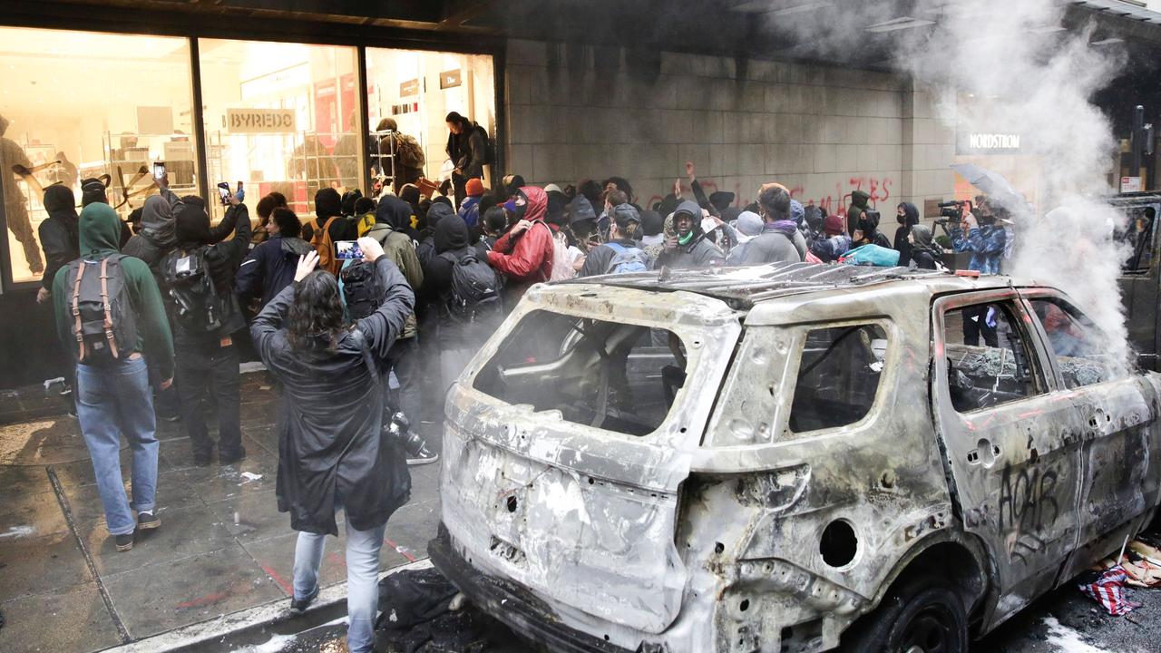 People loot a Nordstrom store near a burnt-out police car following demonstrations in Seattle. Picture: AFP