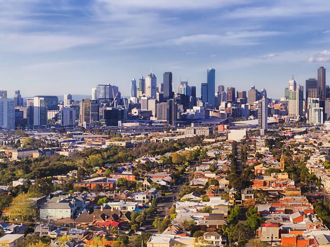 Aerial view of Melbourne city CBD high-rise towers from Port Melbourne and Southbank above residential suburb house roofs and local streets, roads, cars and parks.