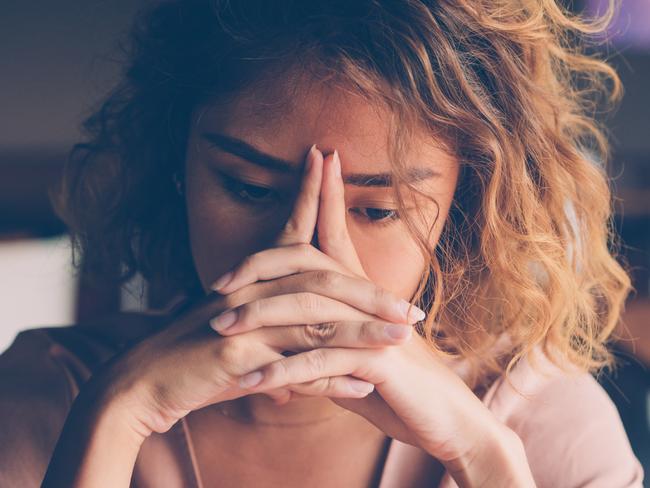 Closeup of sad young Asian woman at cafe leaning head on clasped hands and staring into vacancy. Tired freelancer feeling burnout. Stress and bad news concept