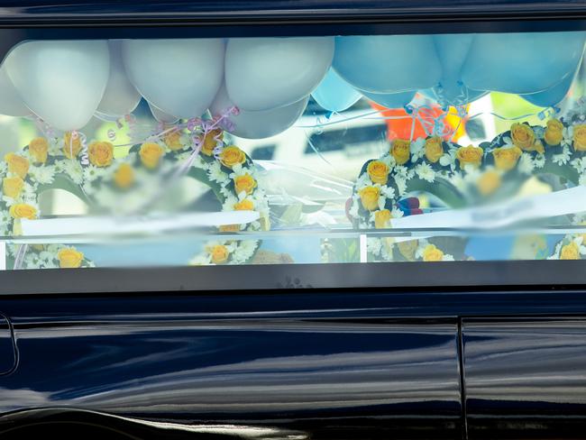 A hearse full of flowers and balloons transports the small coffins.