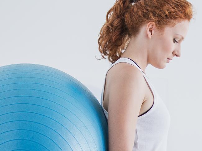 Woman with orthopedic problem exercising with ball while physiotherapist supporting her