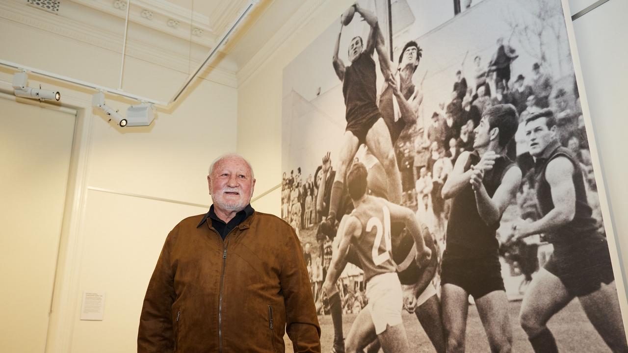 Club champion Graham Molloy stands in front of an almost 4-metre-high image of himself taking a mark at the Norwood Oval in 1969. Norwood footy fans have until the end of the month to soak up a fascinating display of historic memorabilia. Image: Andre Castellucci