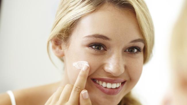 Pretty young woman smiling while applying face cream to her skin cb