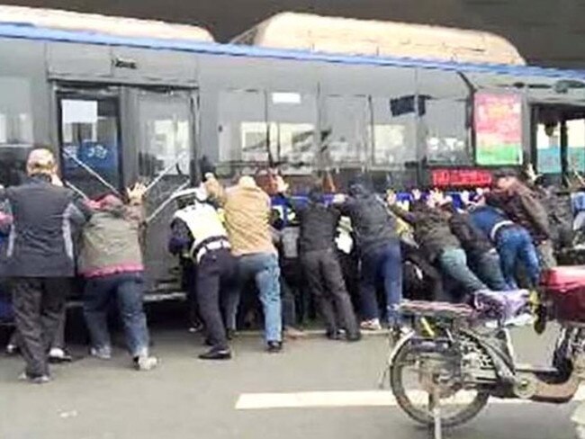 Heave ... Passers-by heed a call to help and begin to lift the bus off the trapped man. Picture: CCTV+ / YouTube