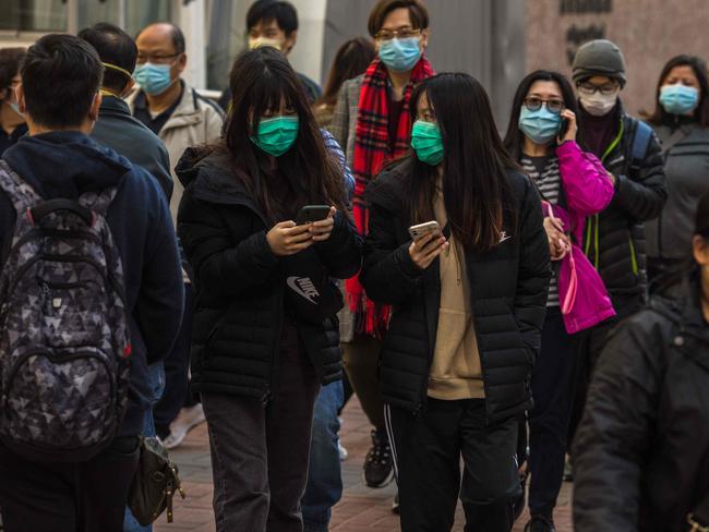 People wearing masks walk along a street in Hong Kong on January 30, 2020, as a preventative measure after a virus outbreak which began in the Chinese city of Wuhan. - Long queues outside of pharmacies and panic buying at supermarkets has become commonplace in Hong Kong in recent days as the crowded metropolis panics over the spread of China's new coronavirus. (Photo by DALE DE LA REY / AFP)