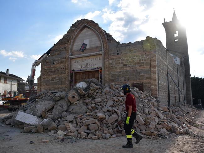 An emergency services worker walks past the ruins of church in San Lorenzo a Flaviano.