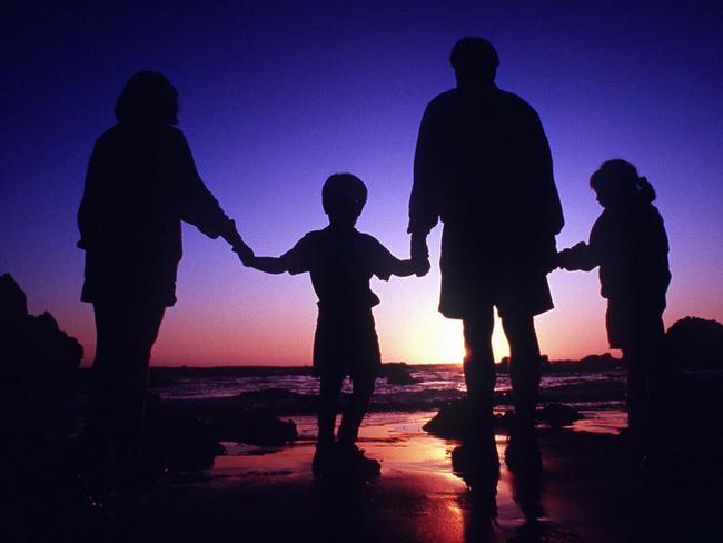 Silhouette of family with parents and children holding hands at the beach.