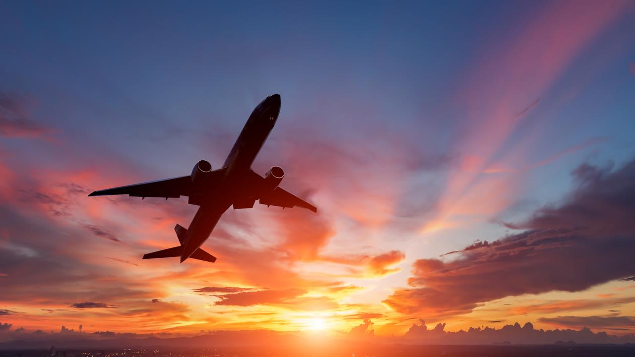 The silhouette of a passenger plane flying in sunset.