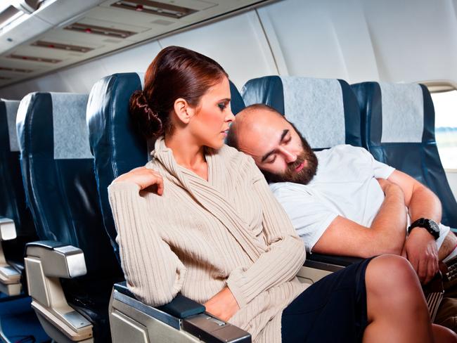 Disgusted woman looking at the sleeping man sitting next to her, who rests his head on her shoulder.