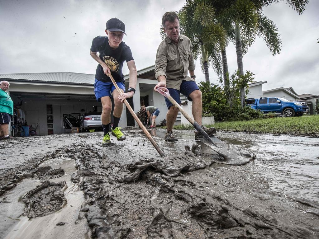 Craig Windel and son Brodie sweep mud from their front drive at their home in Idalia, Townsville. Picture: Glenn Hunt