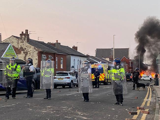 TOPSHOT - Smoke billows from a fire started by protesters as riot police stand guard after disturbances near the Southport Islamic Society Mosque in Southport, northwest England, on July 30, 2024, a day after a deadly child knife attack. Violent clashes broke out in the northern England town where a knife attack claimed the lives of three children, with around 100 protesters lighting fires and battling police. A 17-year-old male suspect from a nearby village arrested shortly after the incident remained in custody, police added, as they warned against speculating about his identity or details of the investigation. (Photo by Roland LLOYD PARRY / AFP)