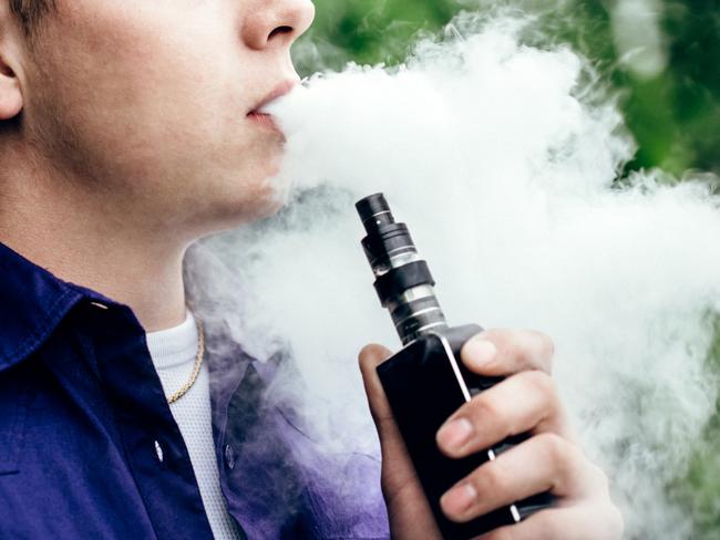 A young adult male has a cloud of nicotine vapor "smoke" pouring from his mouth.  Vape smoking, or "vaping" is growing in popularity, as well as falling under stricter state and governmental regulations.  Horizontal image with copy space.