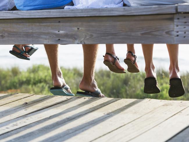 Cropped view of a family with two children sitting on a boardwalk overlooking the beach.  All we see are their legs and feet, wearing sandals and flip flops.