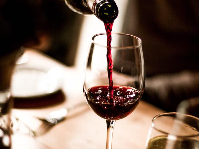 Red wine being poured into a stem glass at the table.