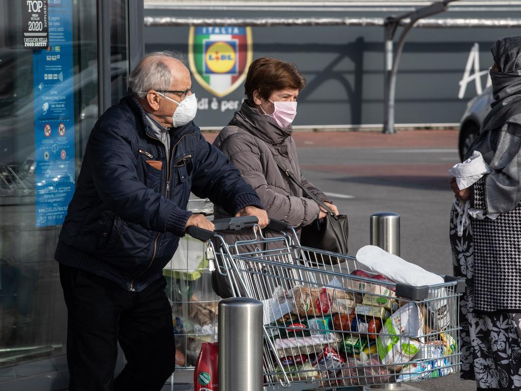 A couple of elderly people wearing respiratory masks push a trolley loaded with foodstuffs after having been given a 10-minutes access to shop in Italy. Picture: Emanuele Cremaschi/Getty Images.