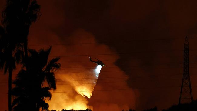 A firefighting helicopter drops water as the Palisades Fire burns toward the Mandeville Canyon. Picture: Getty