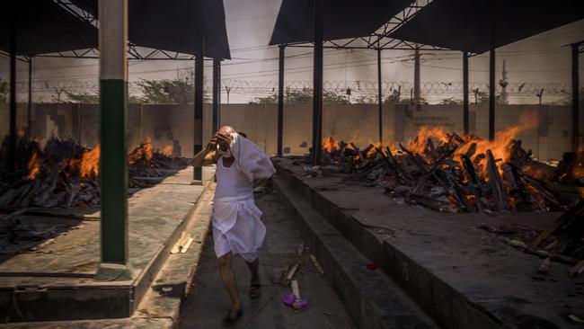 A priest who helps performing last rites, runs while covering his face amid the multiple burning funeral pyres of COVID-19 patients in New Delhi, India. Picture: Getty Images