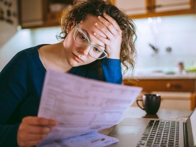 Young brunette curly female reading her bill papers, looking stressed. Picture:  iStock.