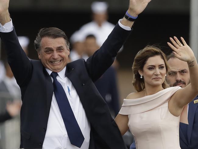 Flanked by first lady Michelle Bolsonaro, Brazil's President Jair Bolsonaro waves as he rides in an open car after his swearing-in ceremony, in Brasilia, Brazil, Tuesday, Jan. 1, 2019. (AP Photo/Andre Penner)