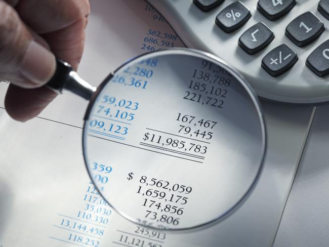 Close up of a man holding a magnifying glass over a financial report. A calculator sits off to the side.