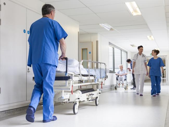 Male nurse pushing stretcher gurney bed in hospital corridor with doctors & senior female patient