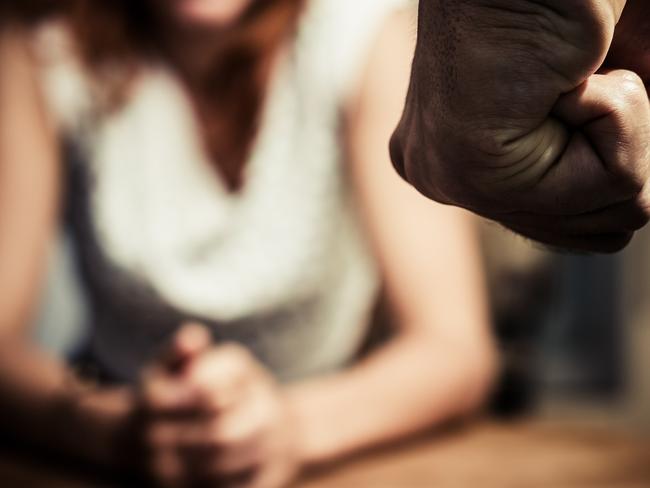 Young woman is sitting hunched at a table at home, the focus is on a man's fist in the foregound of the image