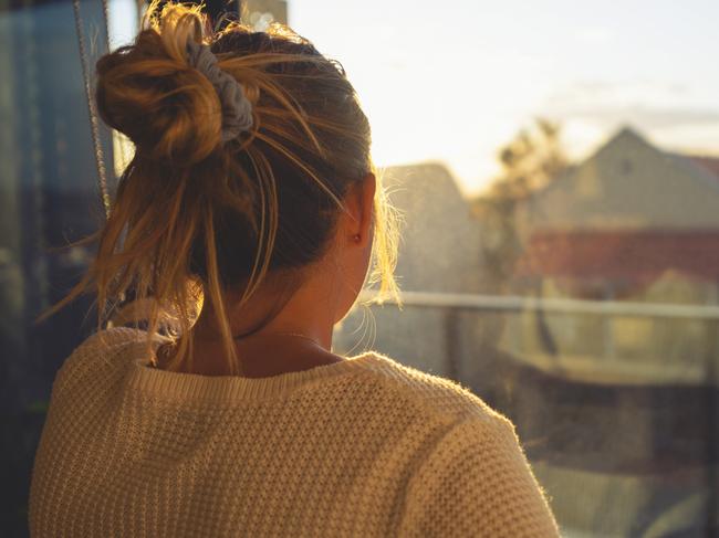 Woman looking through the window at sunset. She is alone and looks a little ad or depressed.