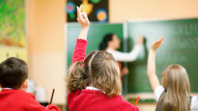 Elementary school kids raising their hands in class to answer a teacher's question.