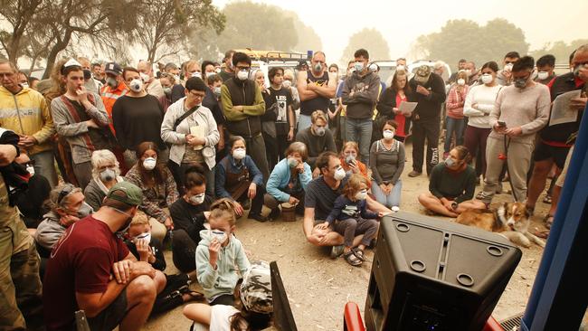 People huddle around a speaker outside the packed town meeting for updates for fire conditions and evacuation procedure from Mallacoota. Picture: David Caird