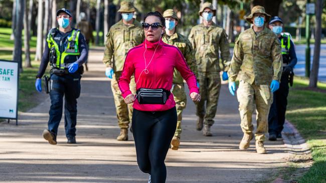 A jogger passes Australian Defence Force personnel and police at the Tan running track in Melbourne on Thursday. Picture: Getty Images