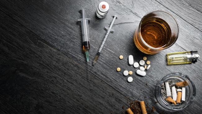 Alcohol or whiskey in a glass, drugs, syringe, cigarettes on a black wood background. Concept of bad habits