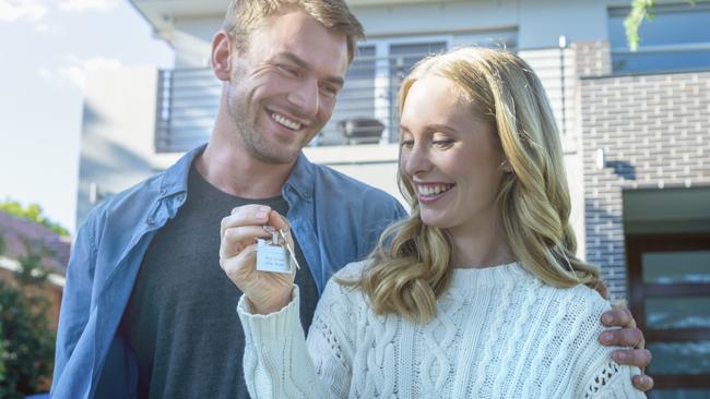 Young couple holding their new house key. They are standing in front of the home in casual clothes. Both are happy, relaxed and smiling. He has a beard and she is blonde. They could be buying or selling real estate. istock