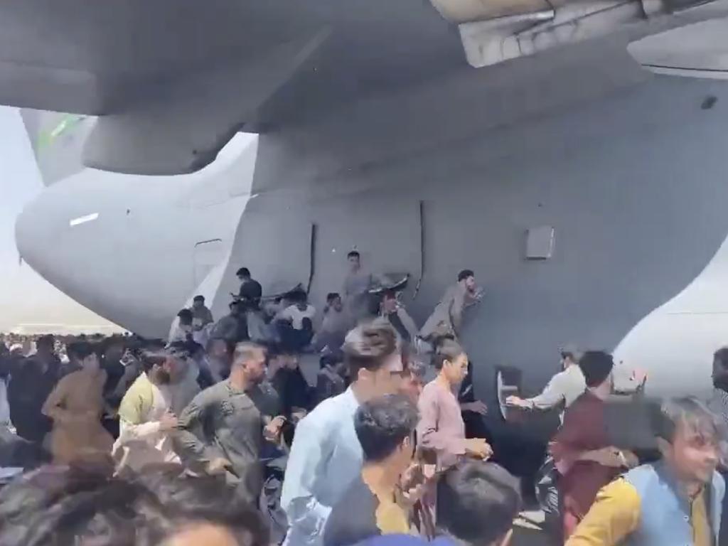 People grab onto a C-17 military aircraft as it attempts to take off at Kabul Airport.