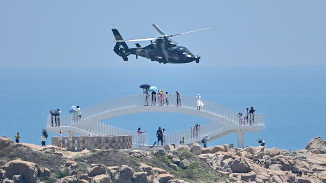 Tourists look on as a Chinese military helicopter flies past Pingtan island ahead of massive military drills off Taiwan following US House Speaker Nancy Pelosi's visit to the self-ruled island. Picture: Hector Retamal/AFP\)