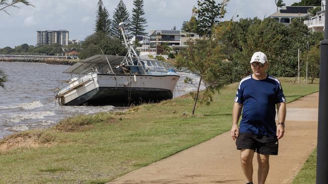 A man on his morning walk passes a fishing trawler washed up on Queens Beach at Redcliffe after ex Tropical Cyclone Alfred crossed the coast. Picture Lachie Millard