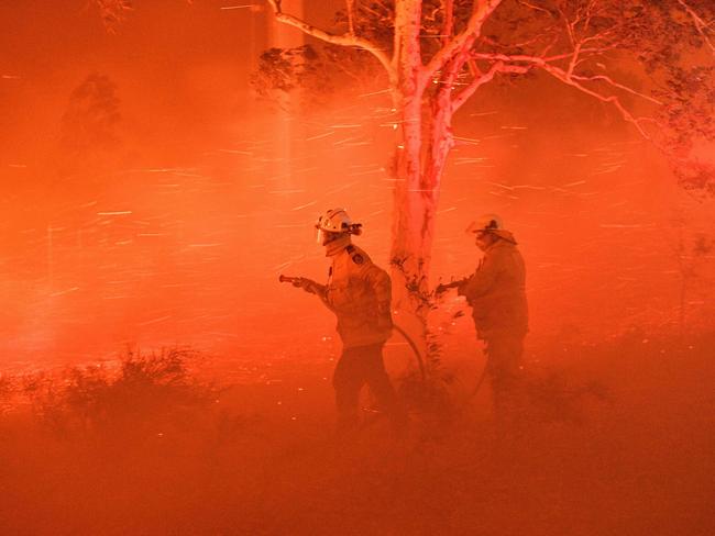 This picture taken on December 31, 2019 shows firefighters struggling against strong winds and flying embers in an effort to secure nearby houses from bushfires near the town of Nowra in the Australian state of New South Wales. - Climate change is already buffeting Australia with more extreme bushfires, droughts and cyclones -- and the fossil-fuel reliant country should brace for worse to come, according to Australia's top science and weather agencies on November 13, 2020. (Photo by Saeed KHAN / AFP)