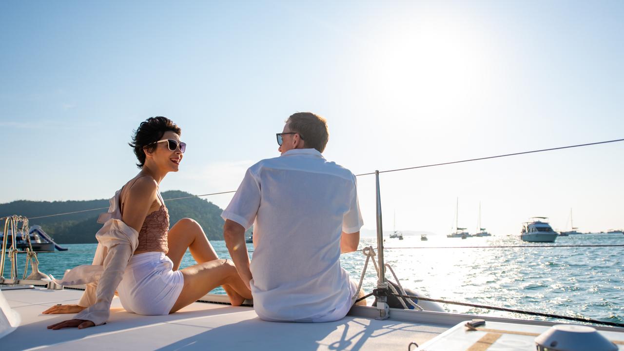 Caucasian couple enjoy outdoor luxury party drinking champagne with talking together while catamaran boat sailing at sunset. Man and woman relax with outdoor lifestyle sail yacht on summer travel vacation; rich couple wealth generic