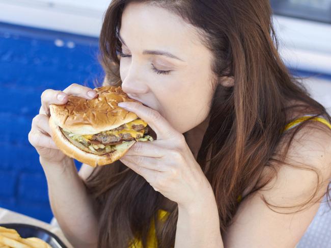 Beautiful young lady eating a tasty burger at an outdoor cafe. Horizontal Shot.