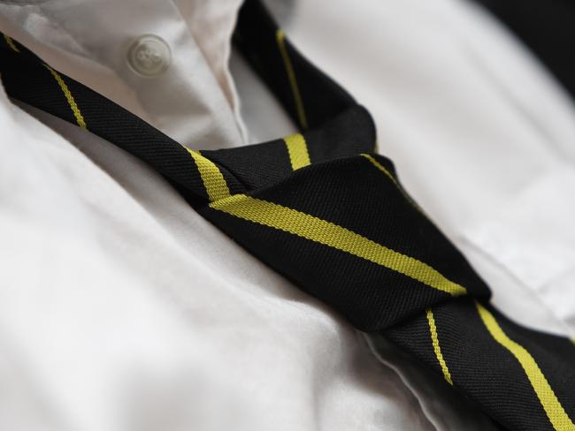 A black tie with yellow stripes worn over a white shirt. Casual appearance. Deliberate selective focus on the knot. Top buttons unfastened.