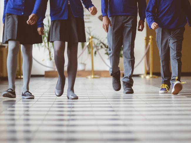 Cropped image of school kids in uniform walking together in a row through corridor. Focus on legs of students walking through school hallway.