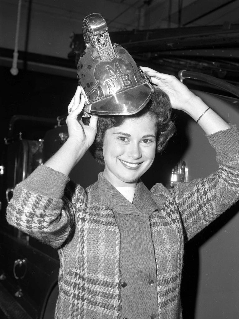 Miss US Fire Station, Carolann Toque, 15, of Los Angeles, tries on a Queensland firefighter's helmet when visiting Brisbane in 1960. Picture: Noel Pascoe