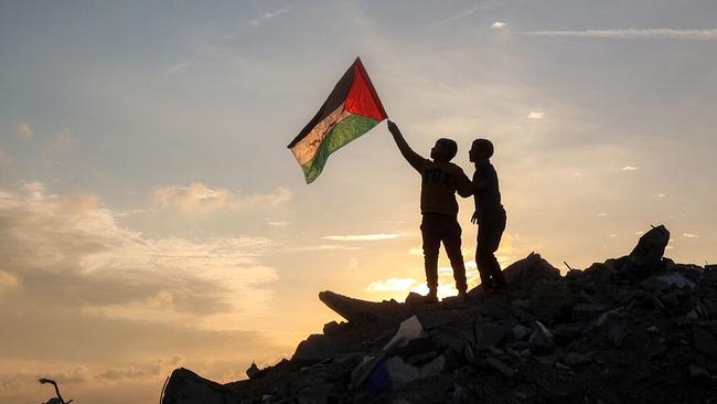 boy runs with a Palestinian flag atop a mound of rubble at a camp for people displaced by conflict in Bureij. Picture: Eyad Baba/AFP