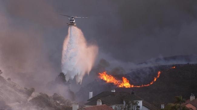 A helicopter drops water around homes threatened by the wind-driven Palisades Fire. Picture: AFP