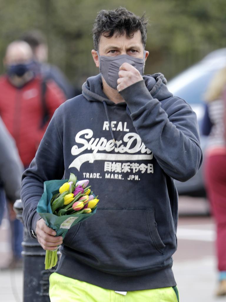 A man wearing a face covering carries flowers at Buckingham Palace. Picture: John Phillips/Getty Images