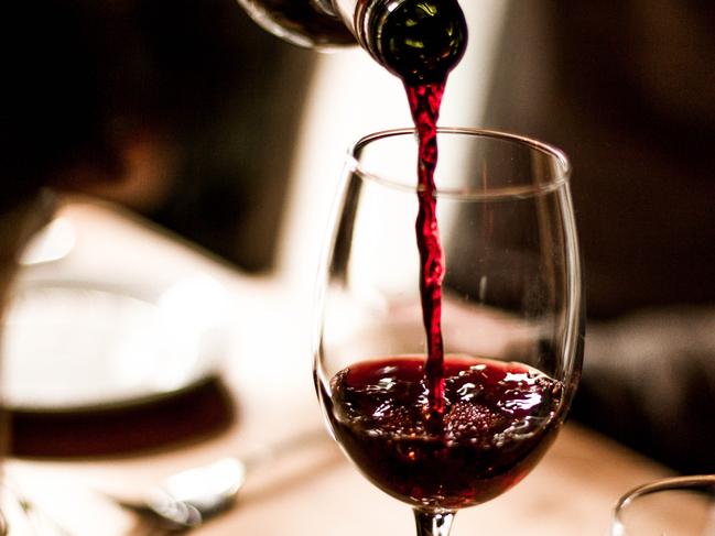 Red wine being poured into a stem glass at the table.