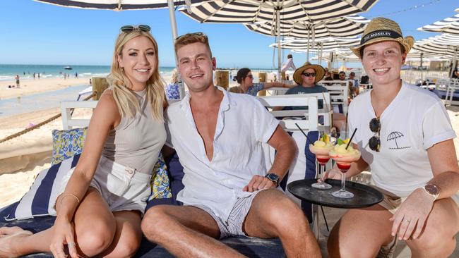 Alice Skocz and Jon Dawson of West Beach enjoying a drink on the sand at the Moseley Beach Club with concierge Olivia Ley. The Beach Club will be open until 6pm on NYE. Pic: Brenton Edwards